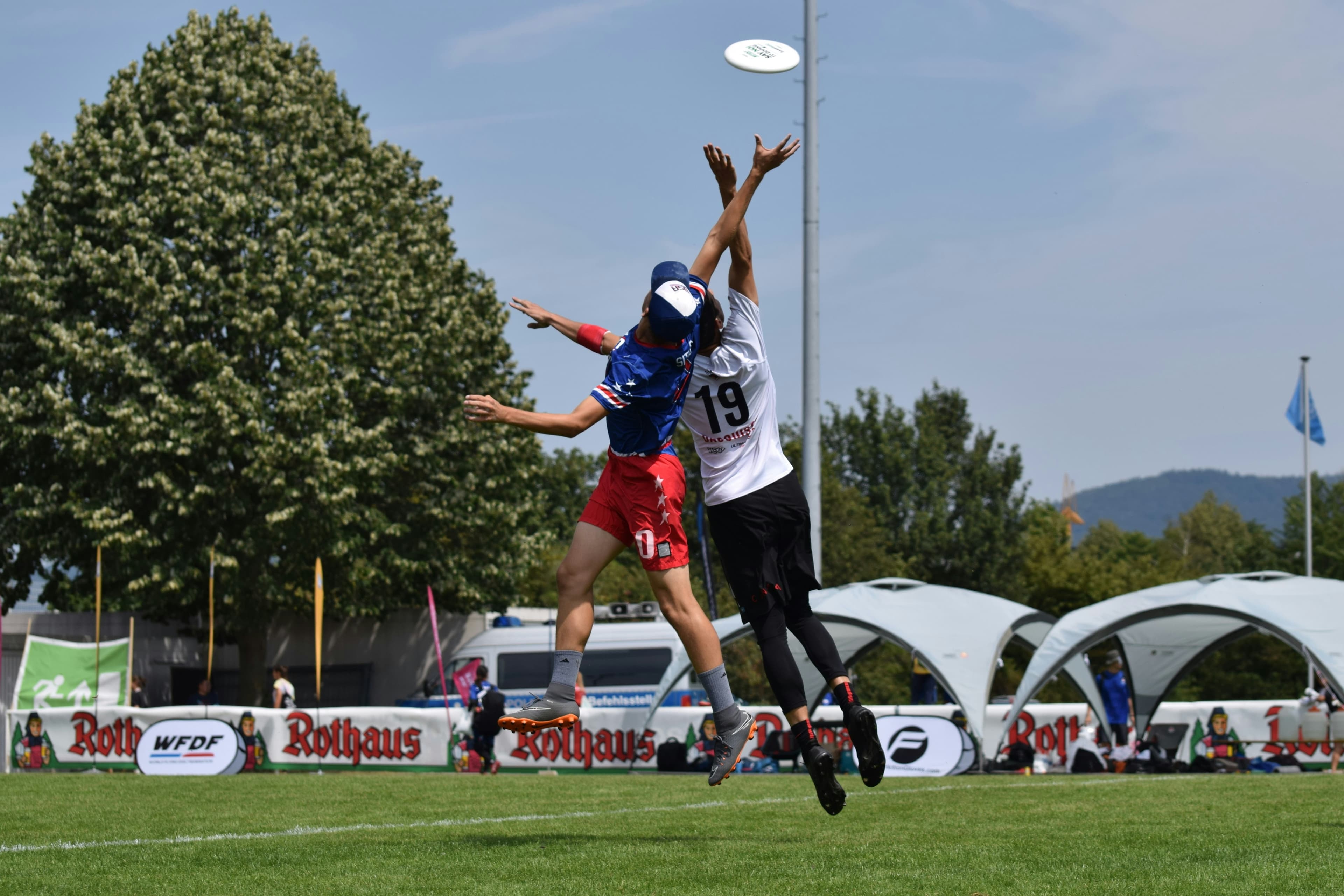 Two Ultimate Frisbee players in a full-extension layout contest for the disc at an outdoor tournament